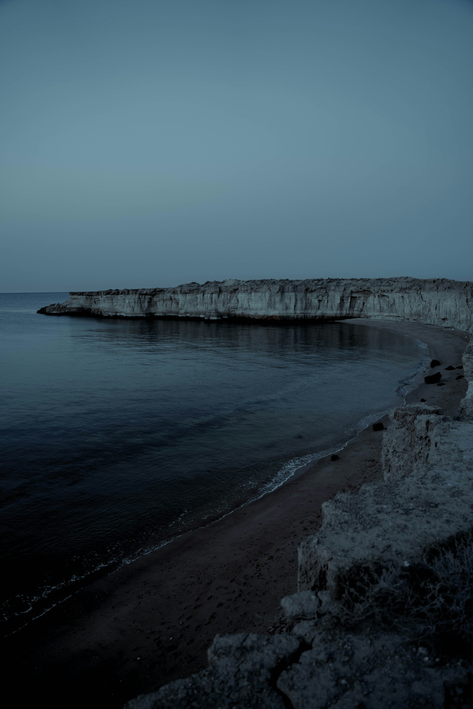 Rocky coastal cliff beside calm water at dusk